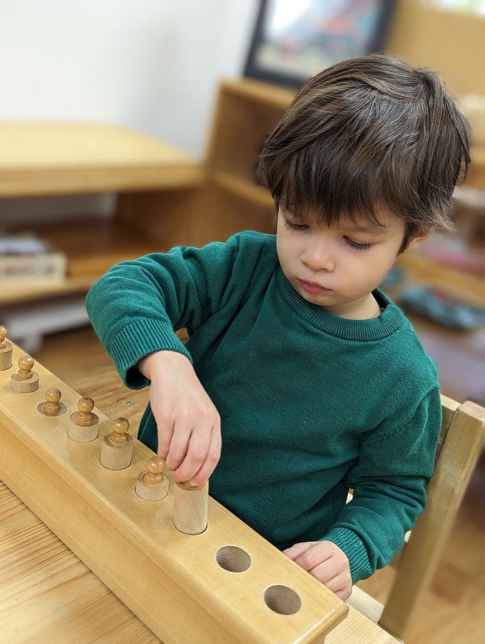 A young boy is playing with a wooden toy on a table.