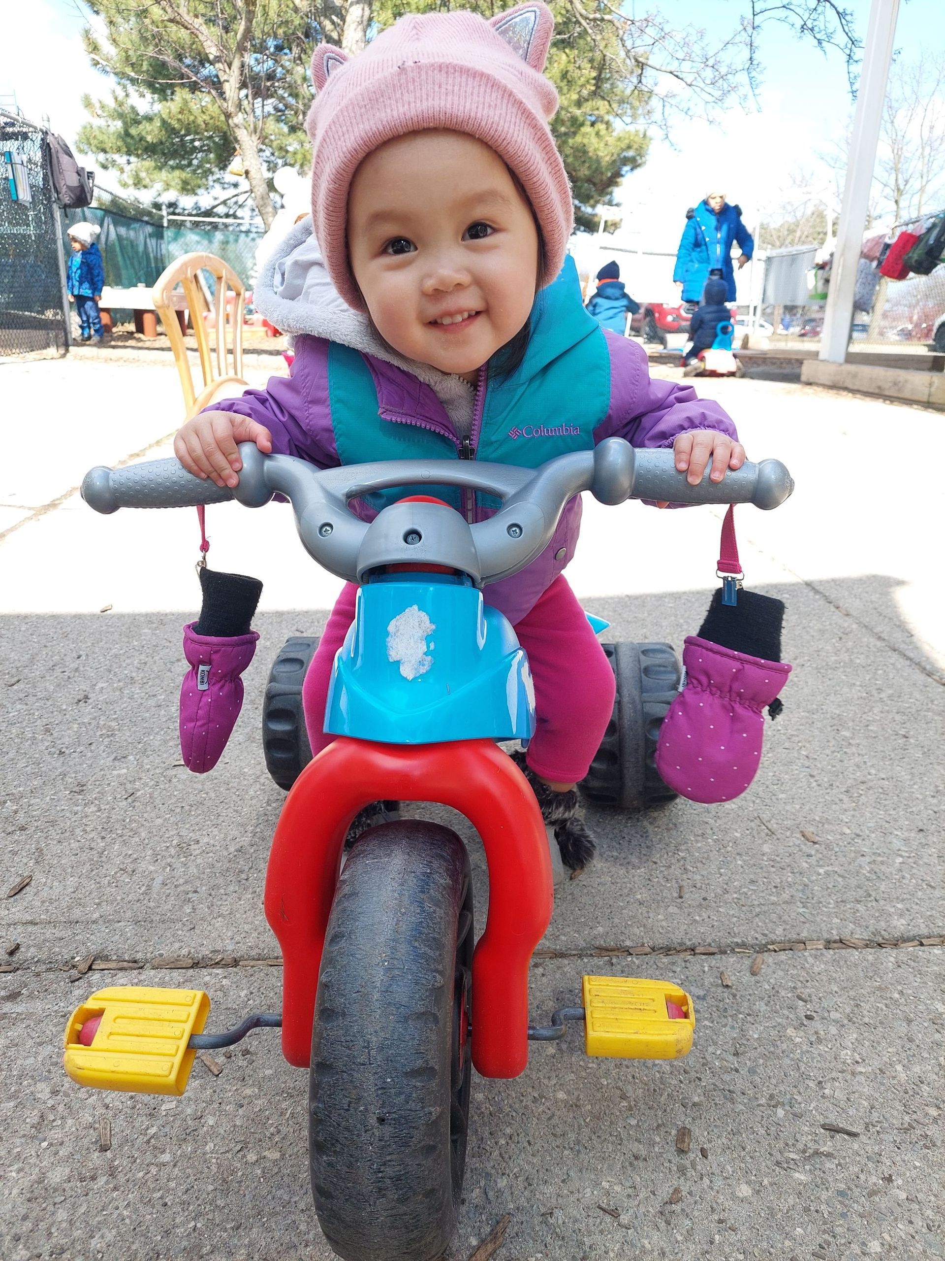 A little girl in a pink hat is riding a tricycle