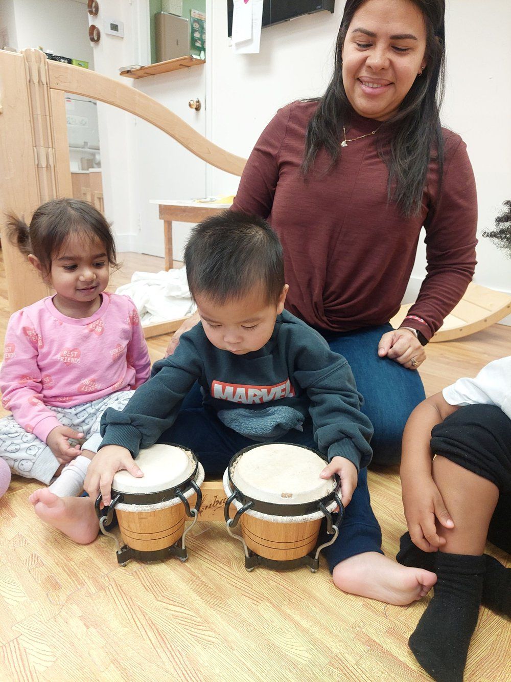 A woman is sitting on the floor with two children playing drums.