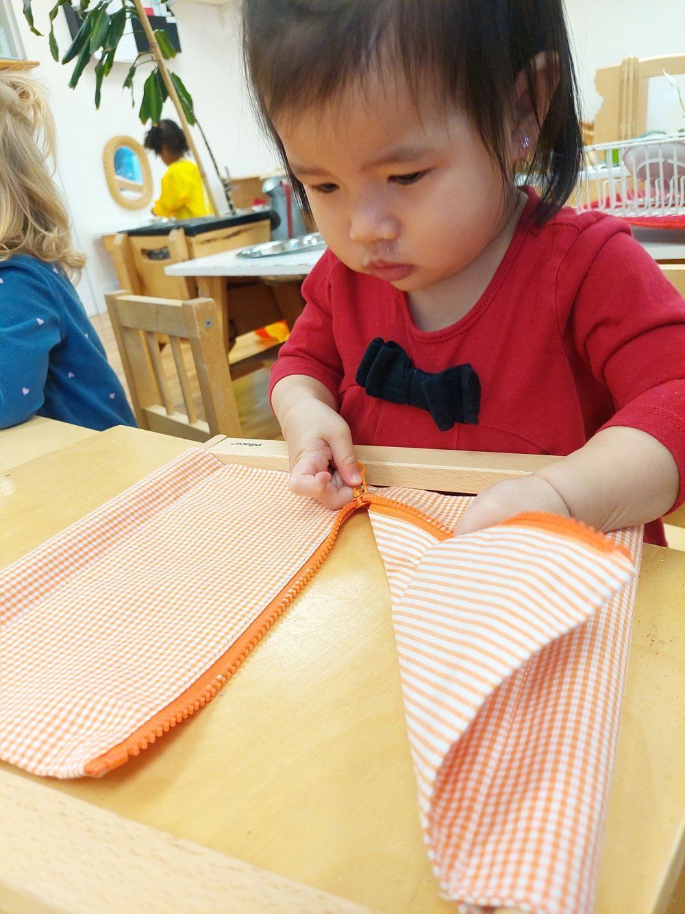A little girl is sitting at a table playing with a piece of fabric.
