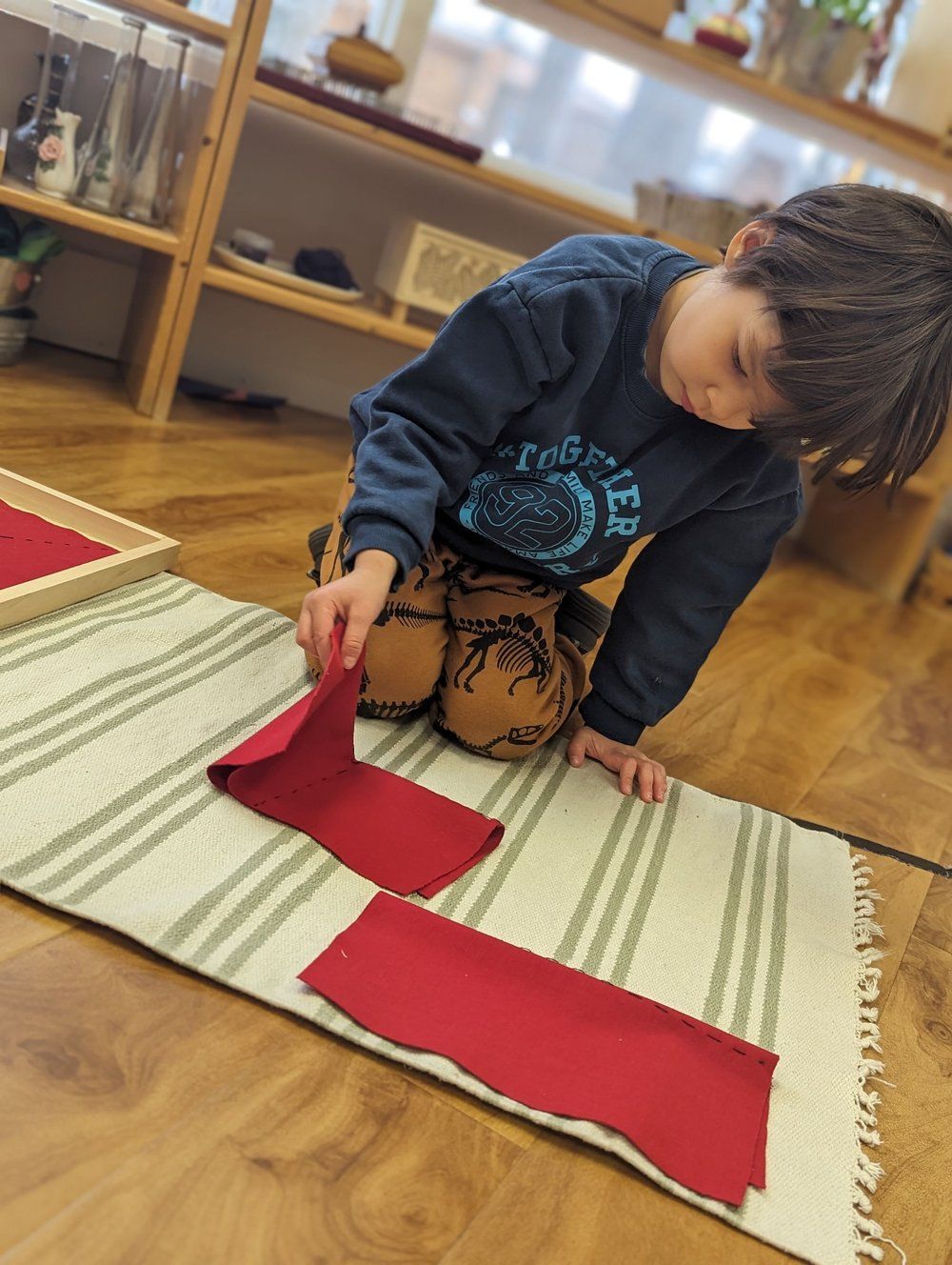 A young boy is sitting on the floor playing with a piece of red fabric.
