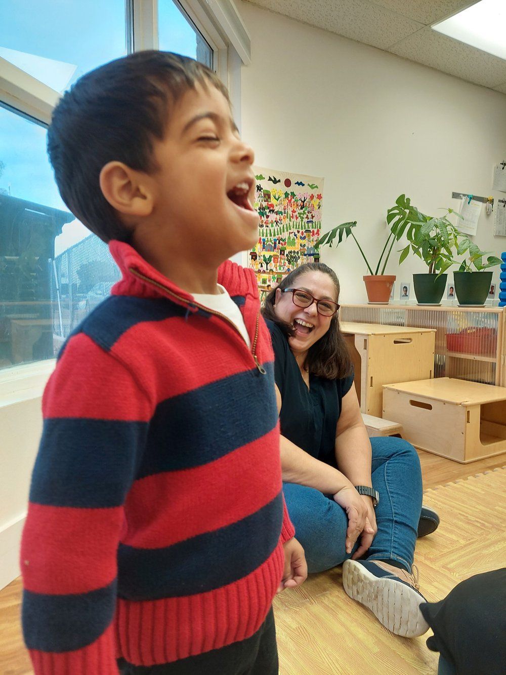 A woman sits on the floor next to a boy who is laughing