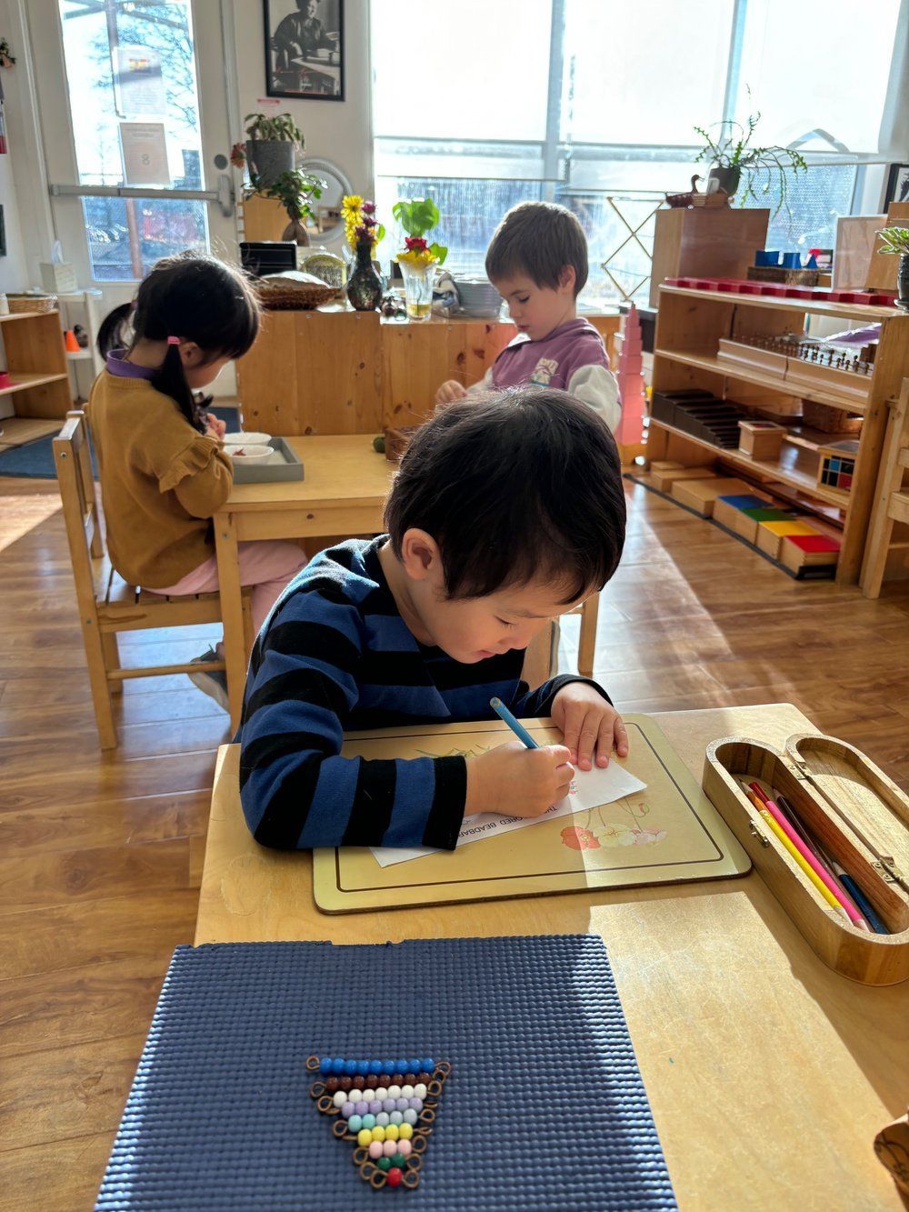 A boy is sitting at a desk in a classroom writing on a piece of paper.