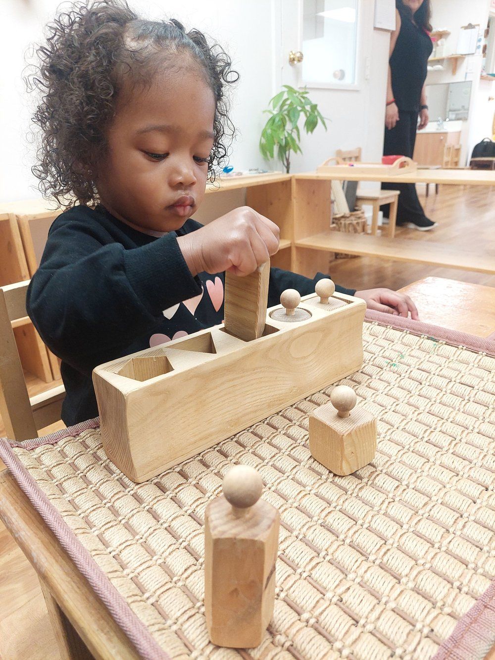 A little girl is playing with wooden blocks on a table.