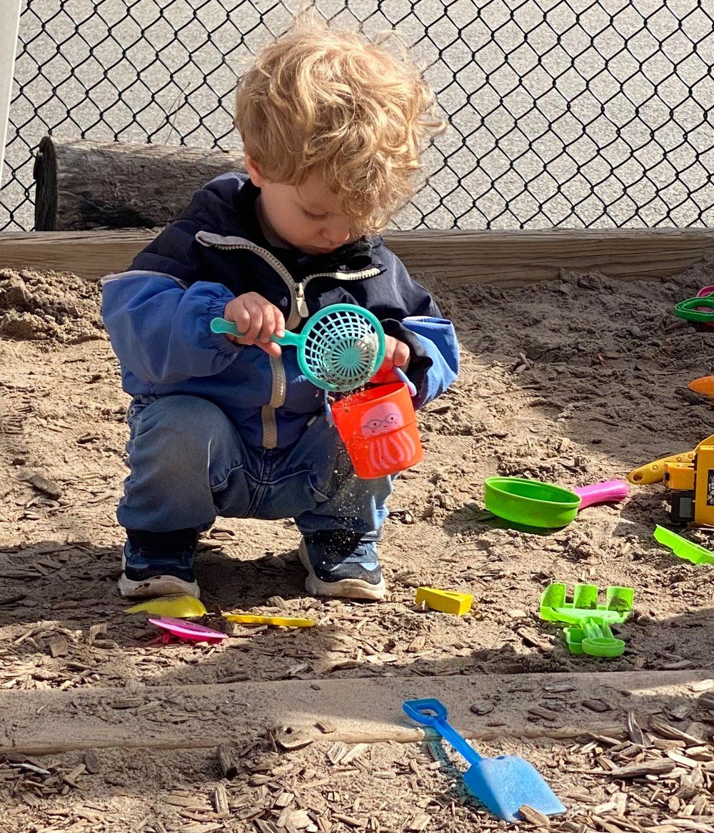 A young boy is playing in a sandbox with toys.