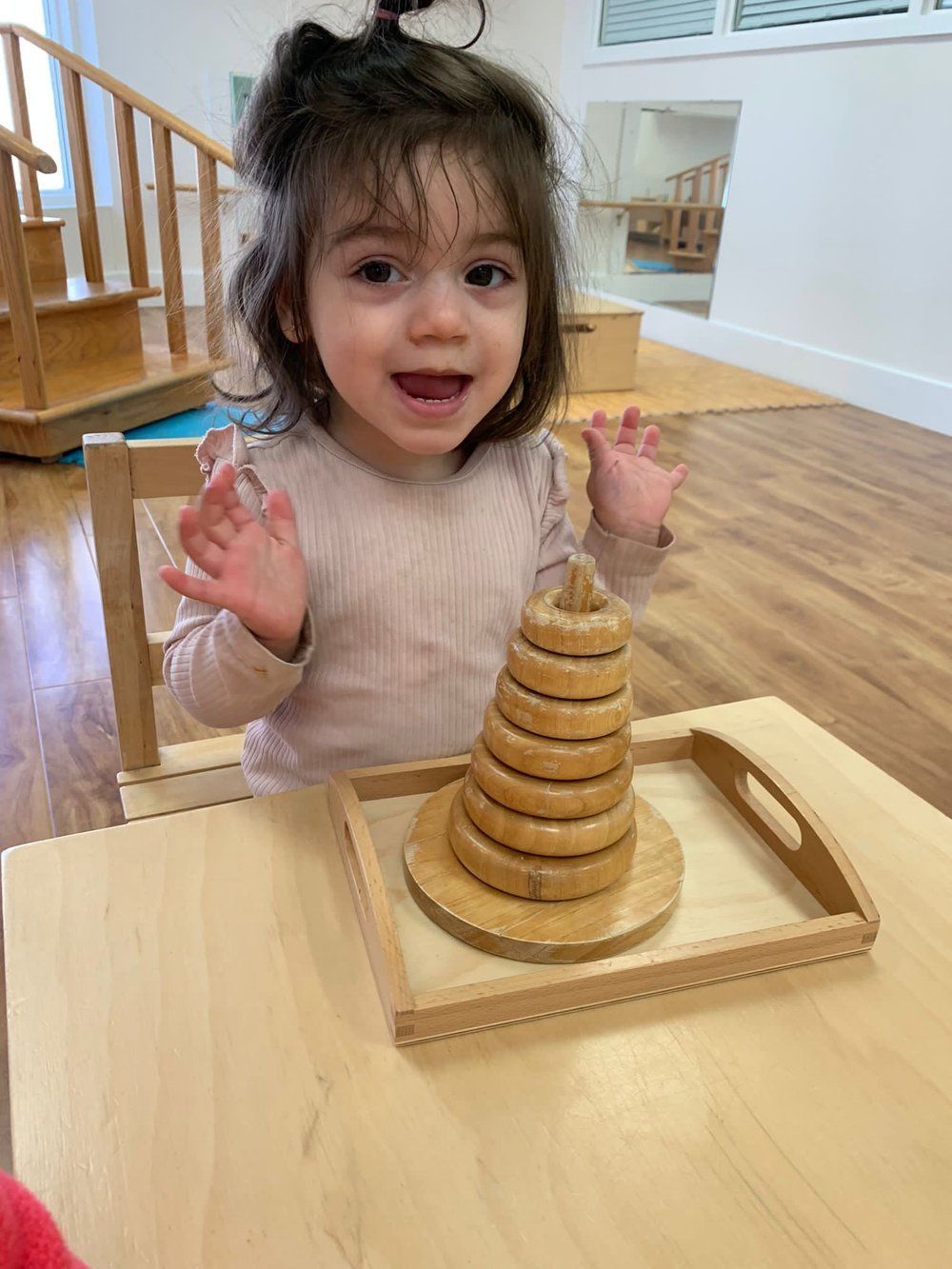 A little girl is sitting at a table playing with a wooden toy.