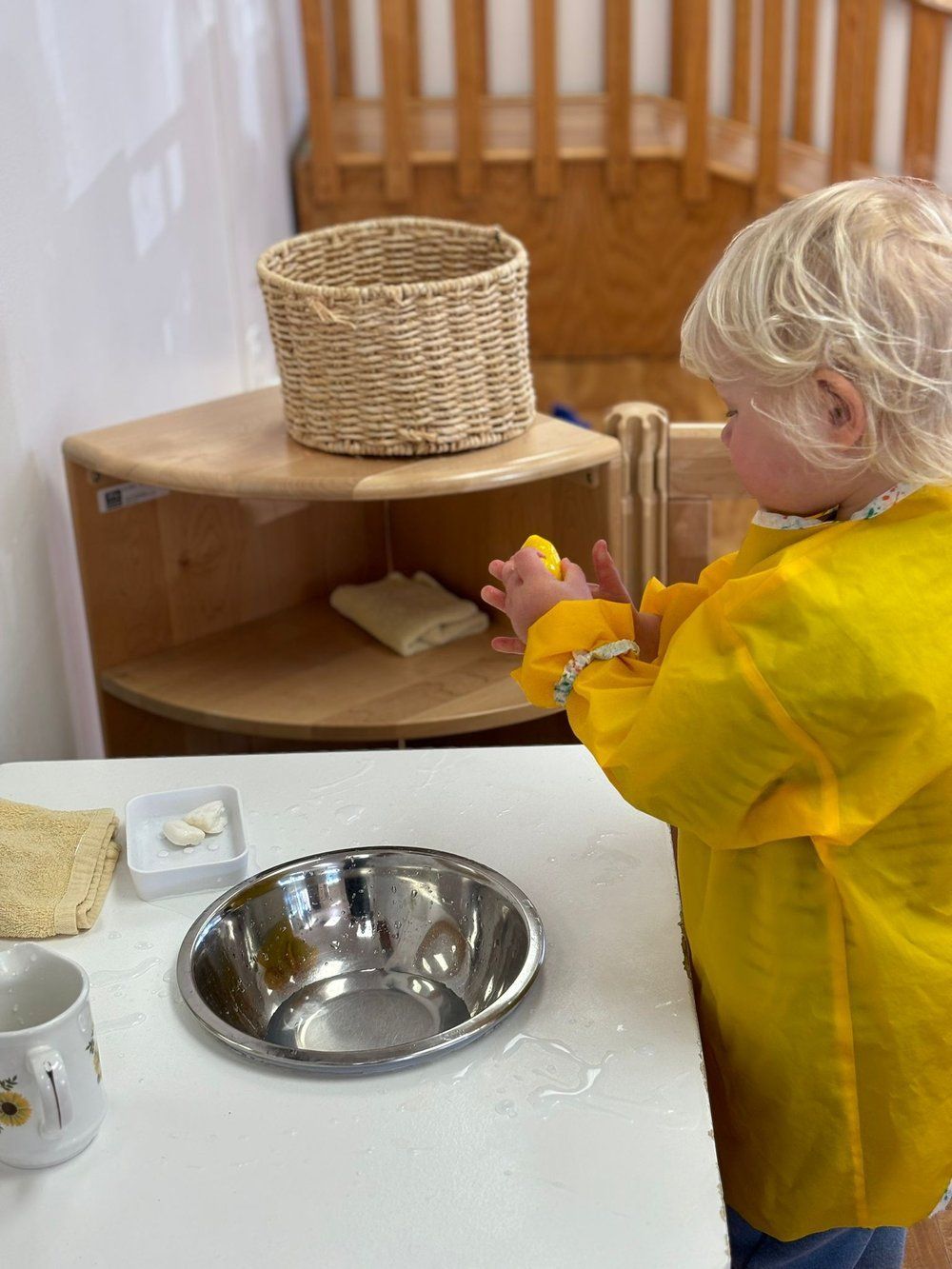 A little girl in a yellow apron is washing her hands in a sink.