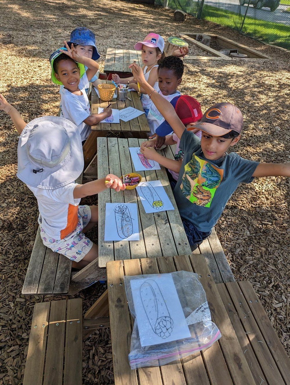 A group of young children are sitting at a wooden picnic table.
