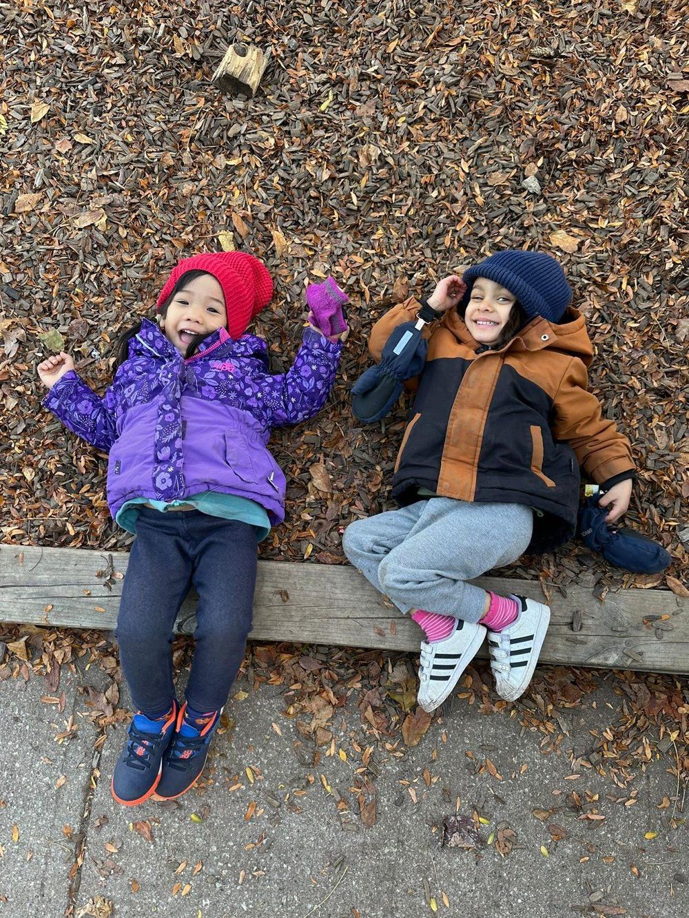 A boy and a girl are laying on a pile of leaves.