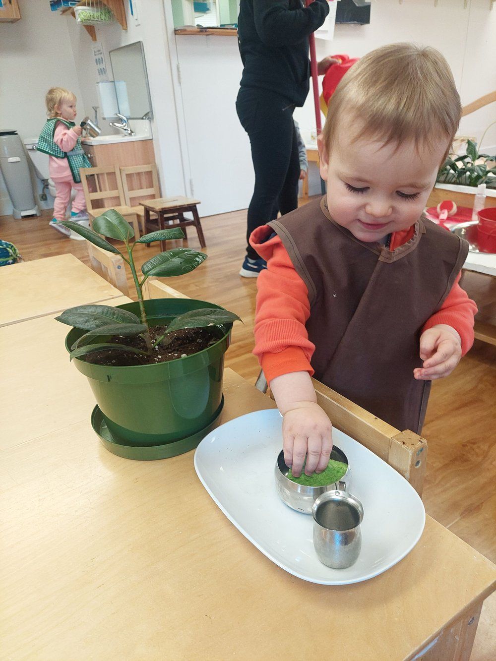 A little boy is playing with a potted plant on a table.