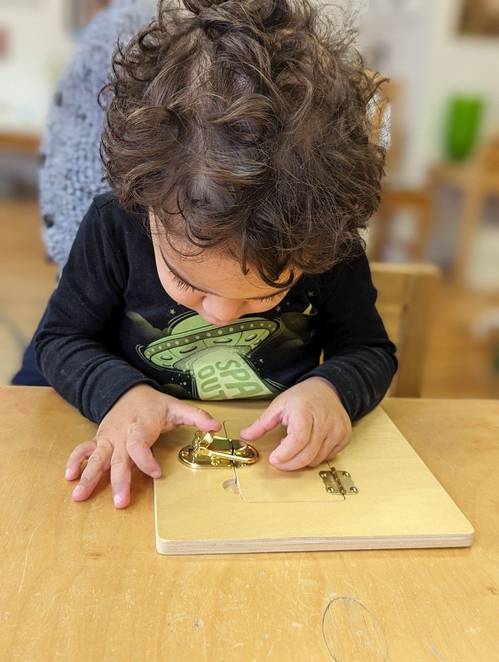 A young boy is sitting at a table playing with a wooden board.