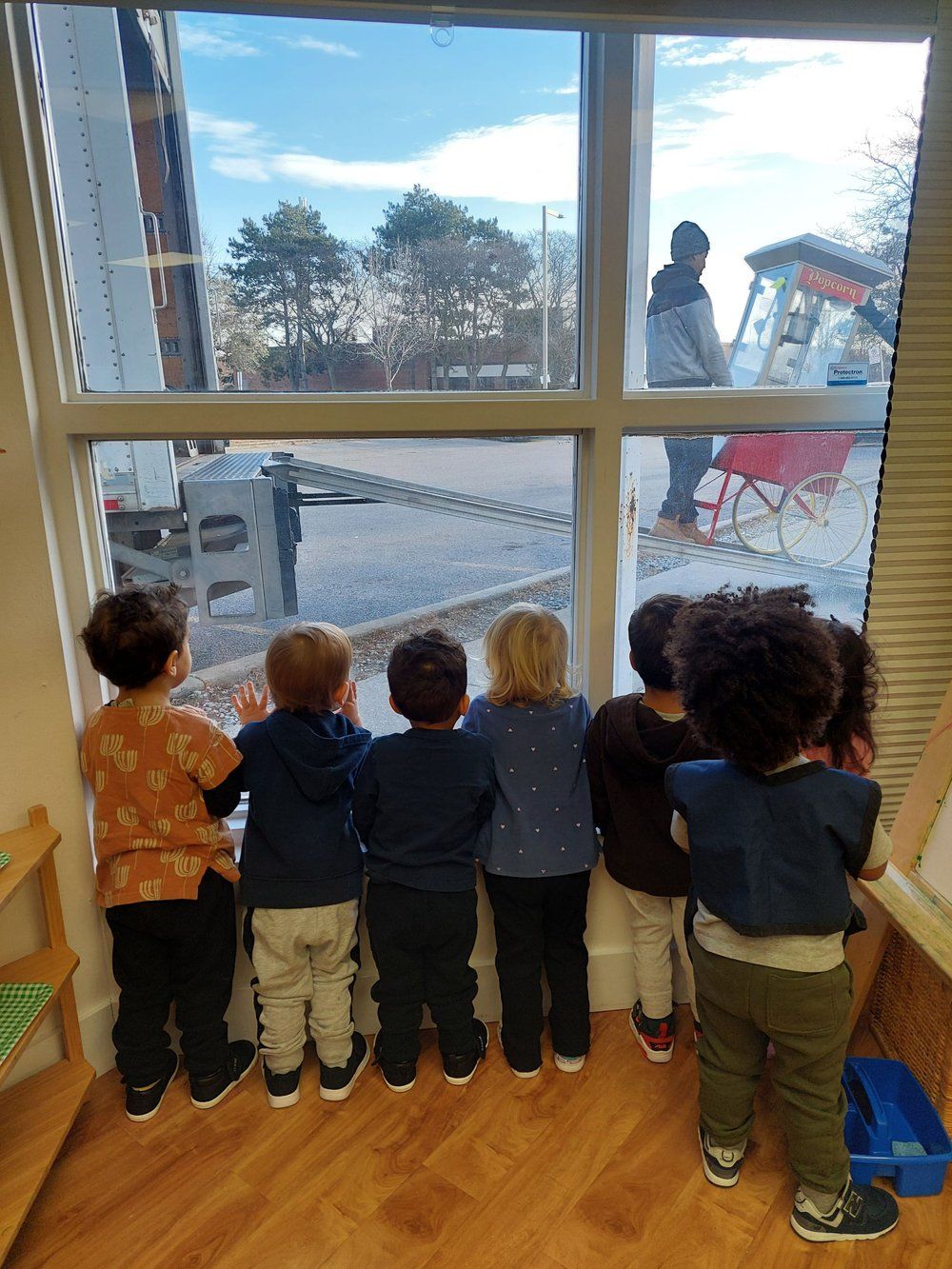 A group of children are standing in front of a window looking out.