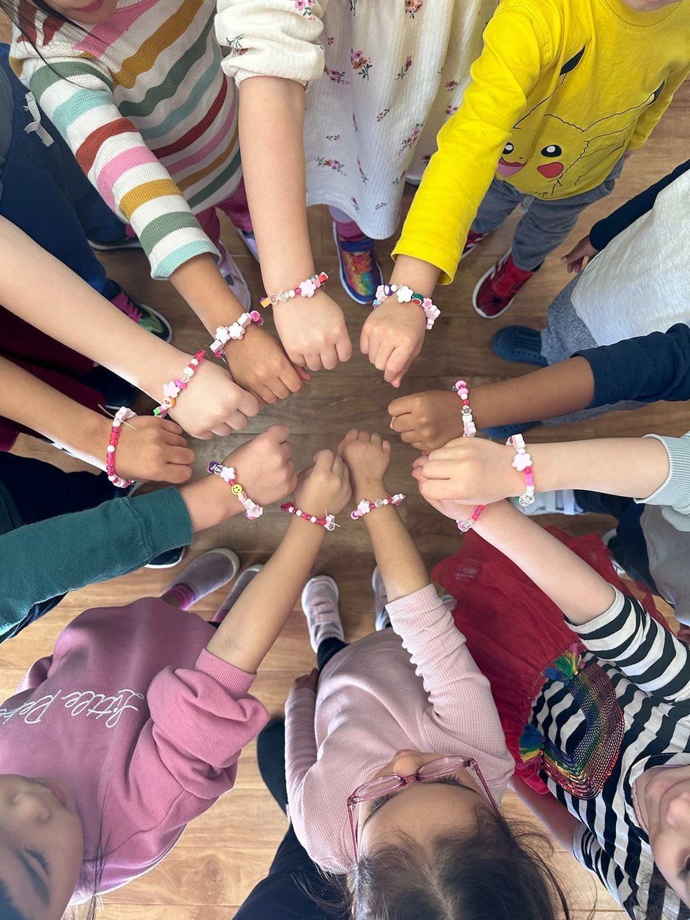 A group of children are holding hands in a circle and wearing bracelets on their wrists.