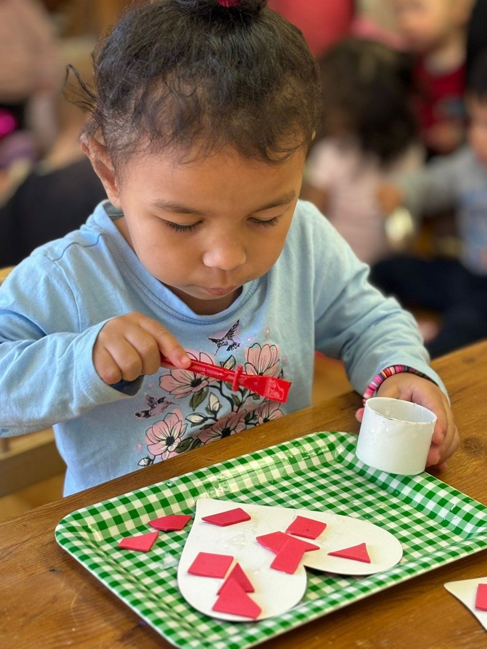 A little girl is sitting at a table making a heart out of paper.