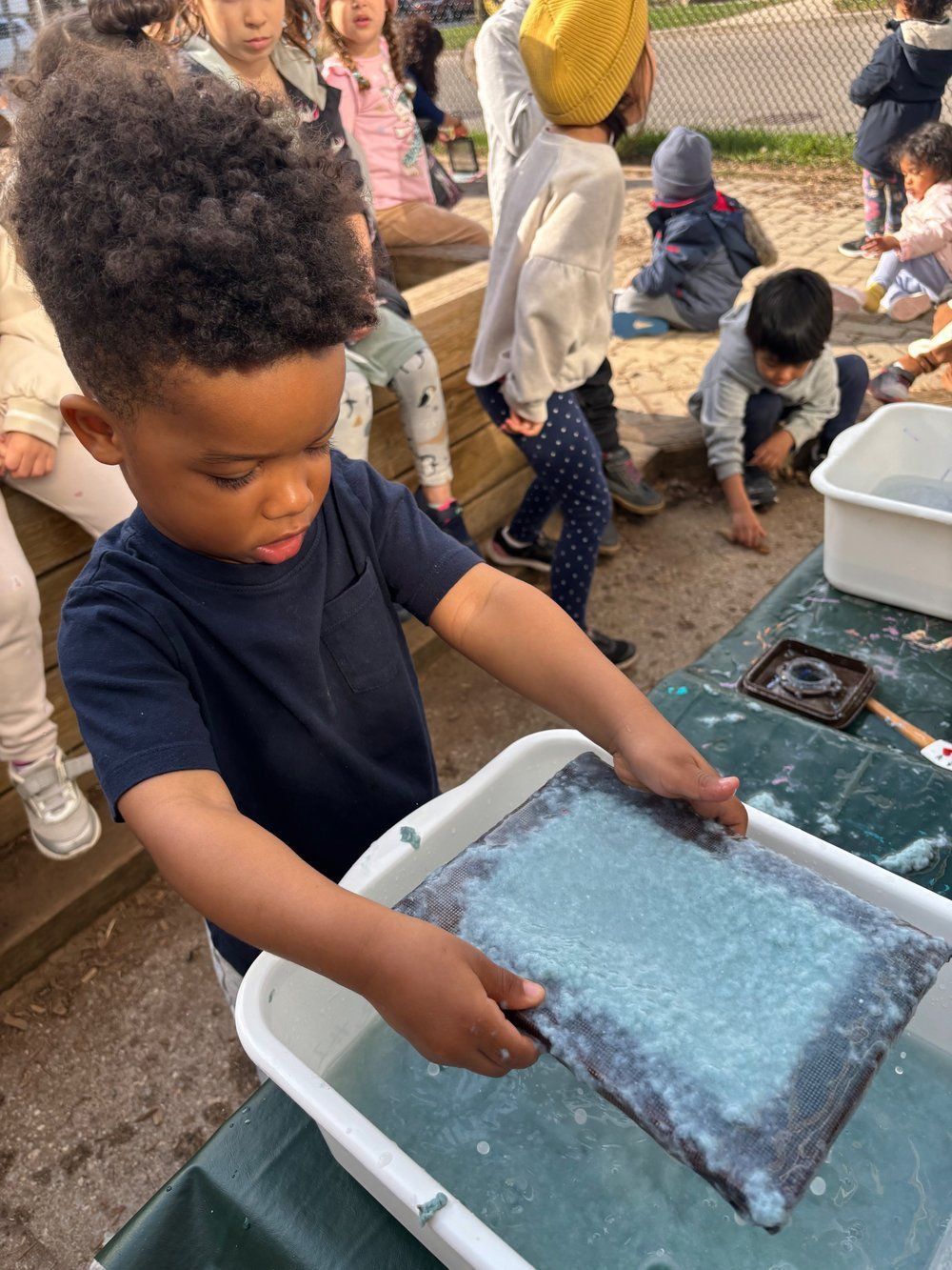 A young boy is playing with a tray of water and a piece of paper.