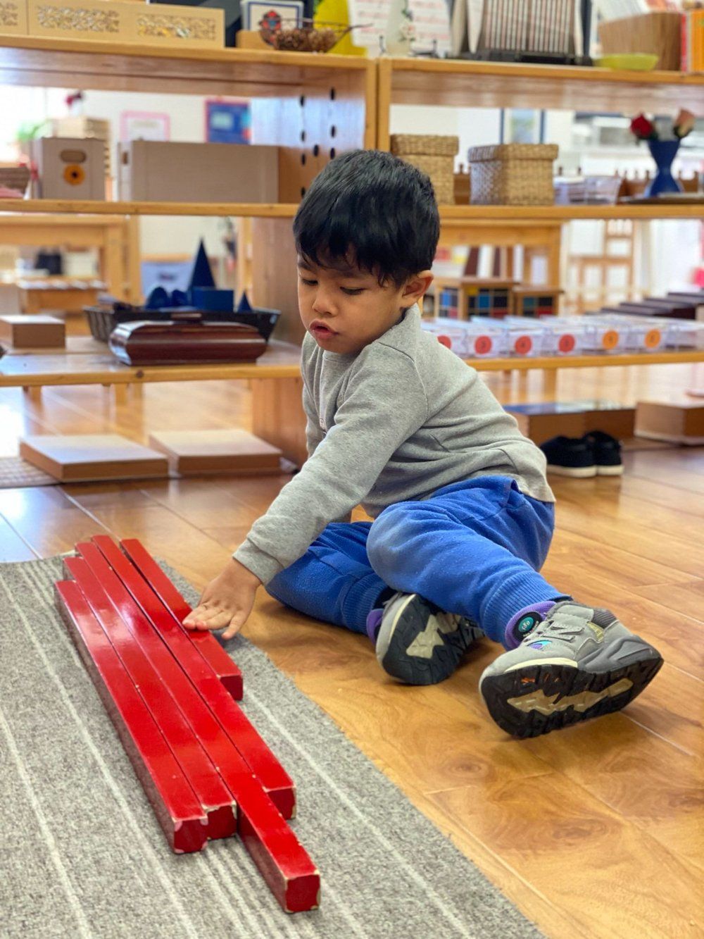 A young boy is sitting on the floor playing with red sticks.