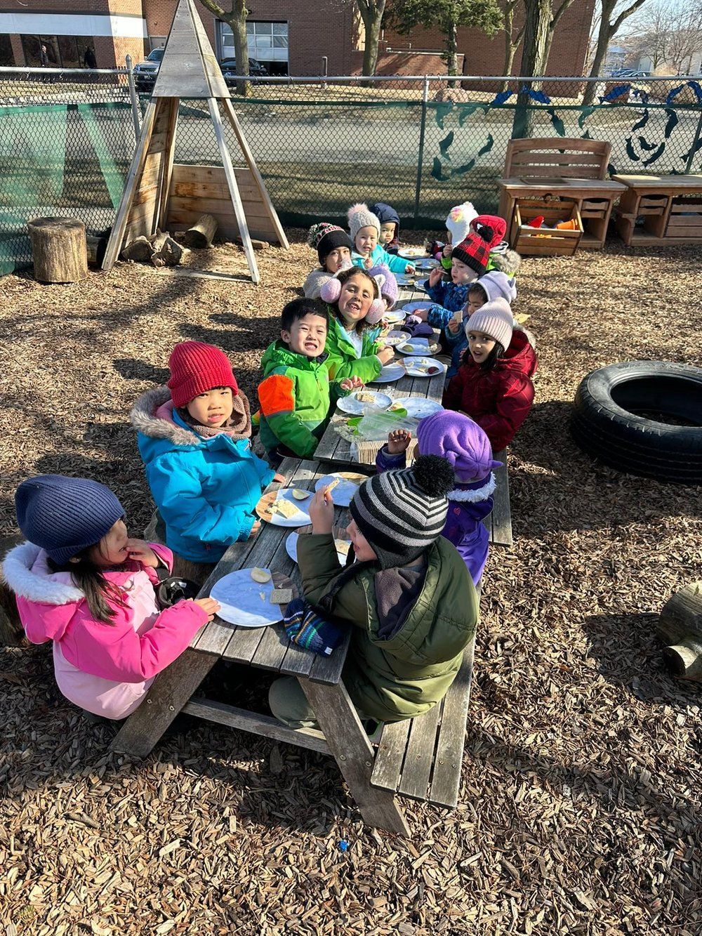 A group of children are sitting at a long picnic table eating food.