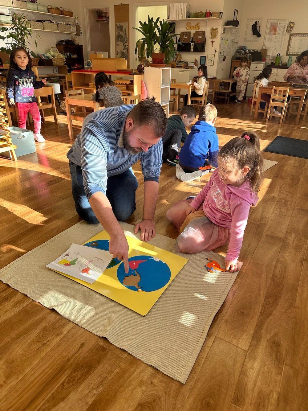 A man and a girl are playing with a map of the world in a classroom.