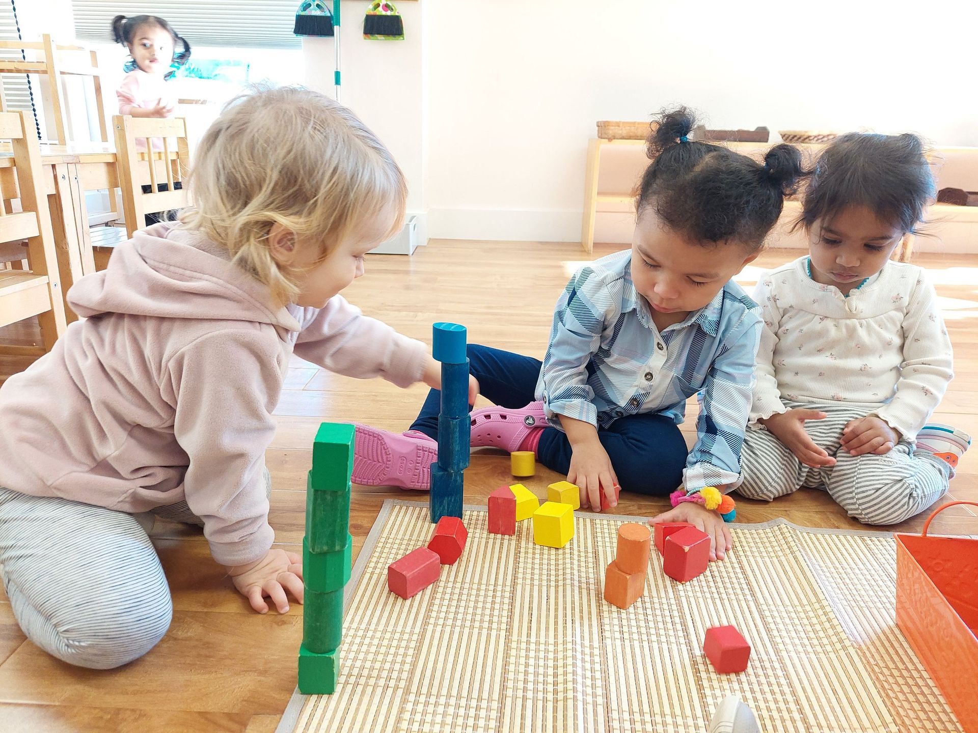 Three young girls are playing with wooden blocks on the floor.