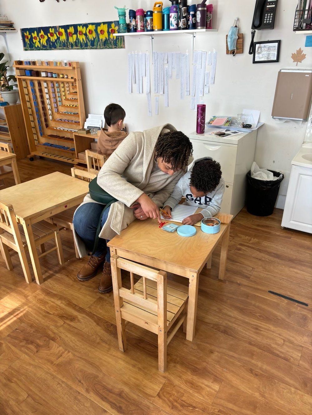 A woman is sitting at a table with a child in a classroom.