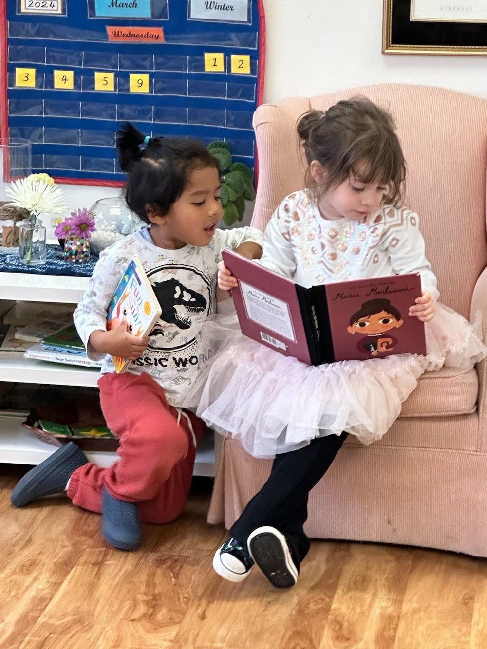 Two little girls are sitting in chairs reading books.