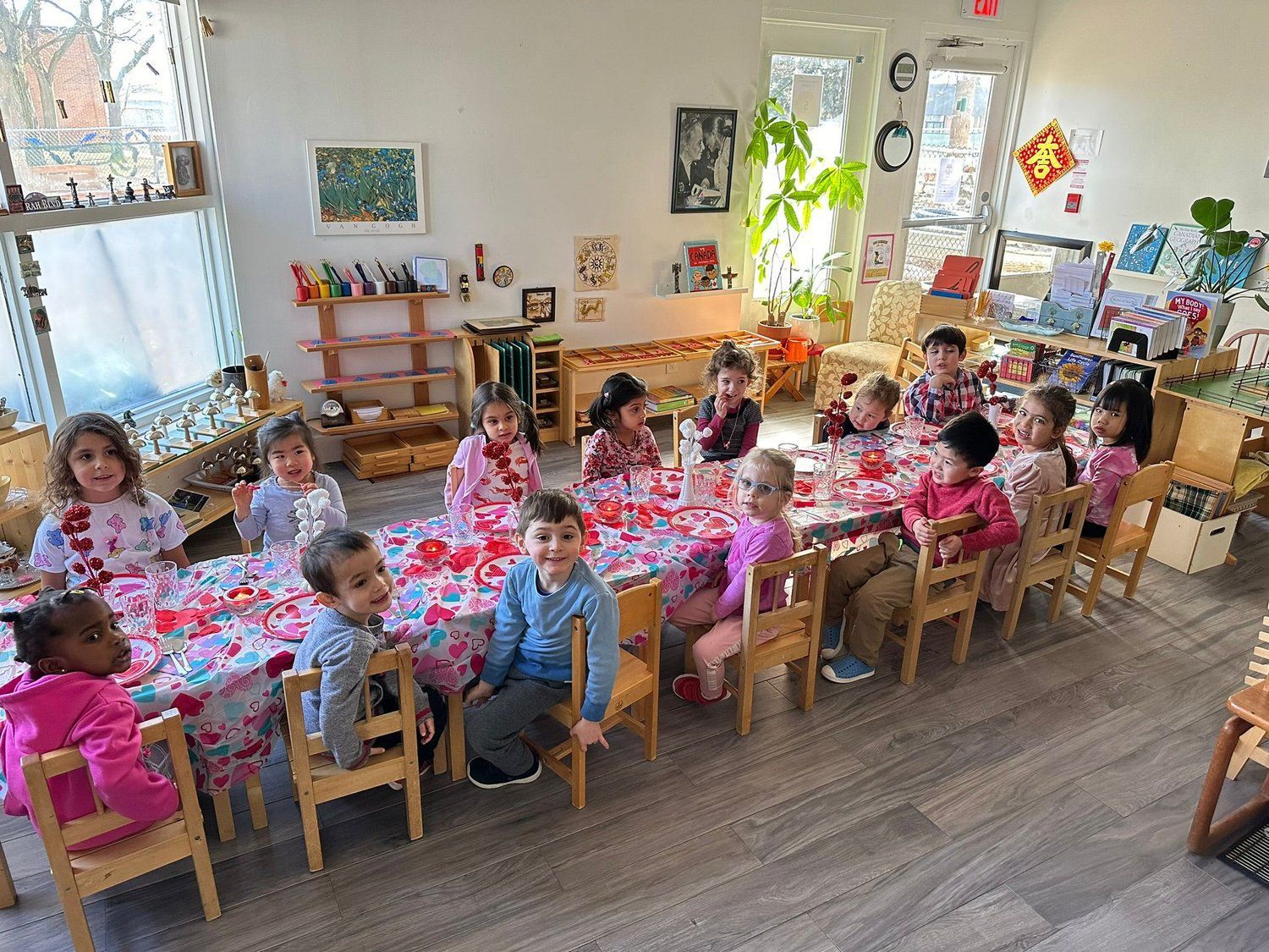 A group of children are sitting at a long table in a classroom.