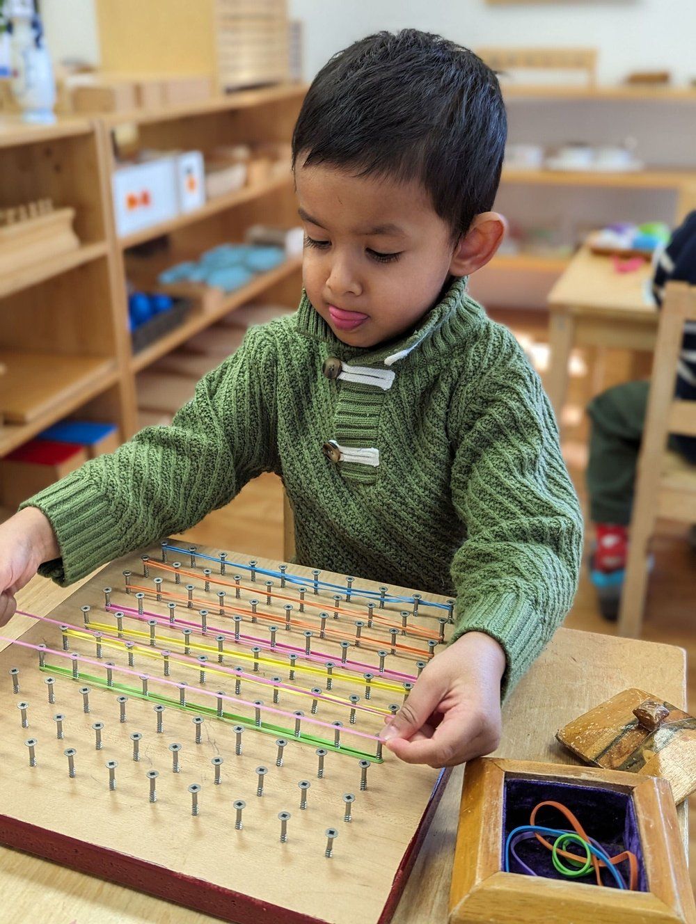 A young boy in a green sweater is playing with a wooden board.
