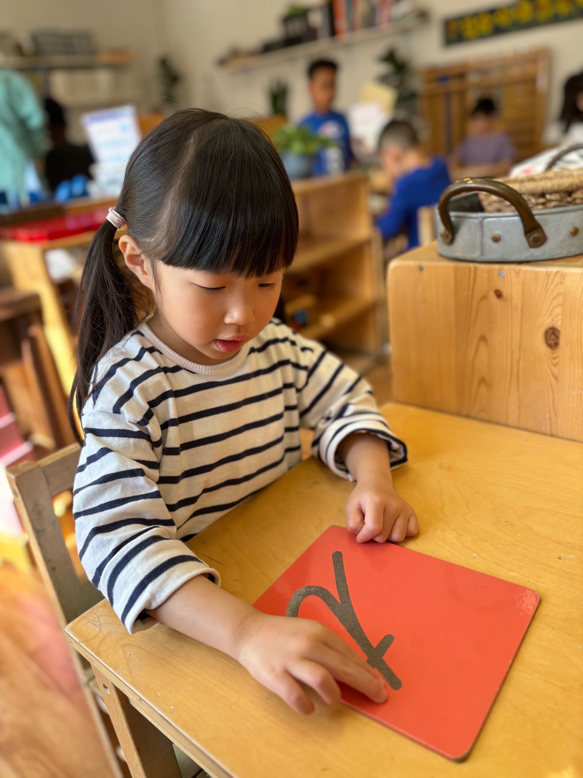 A little girl is sitting at a table playing with a red board.