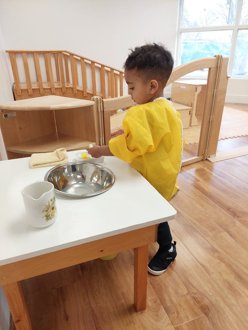 A young boy in a yellow apron is playing with a bowl on a table.