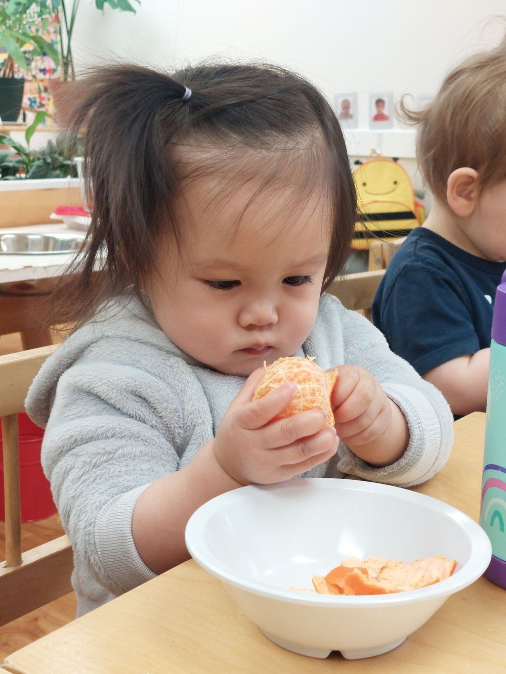 A little girl is sitting at a table eating an orange