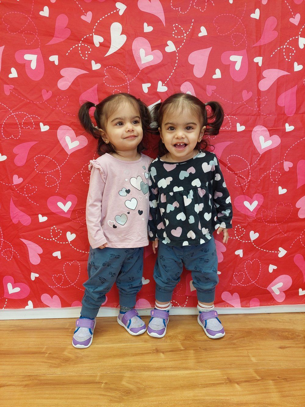 Two little girls are standing next to each other in front of a valentine 's day backdrop.