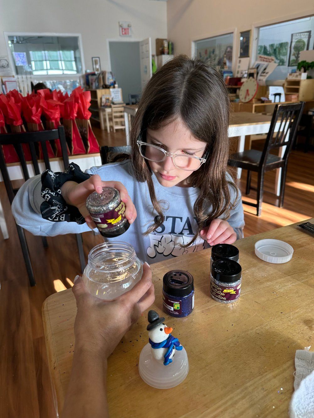 A little girl is sitting at a table making a snow globe.