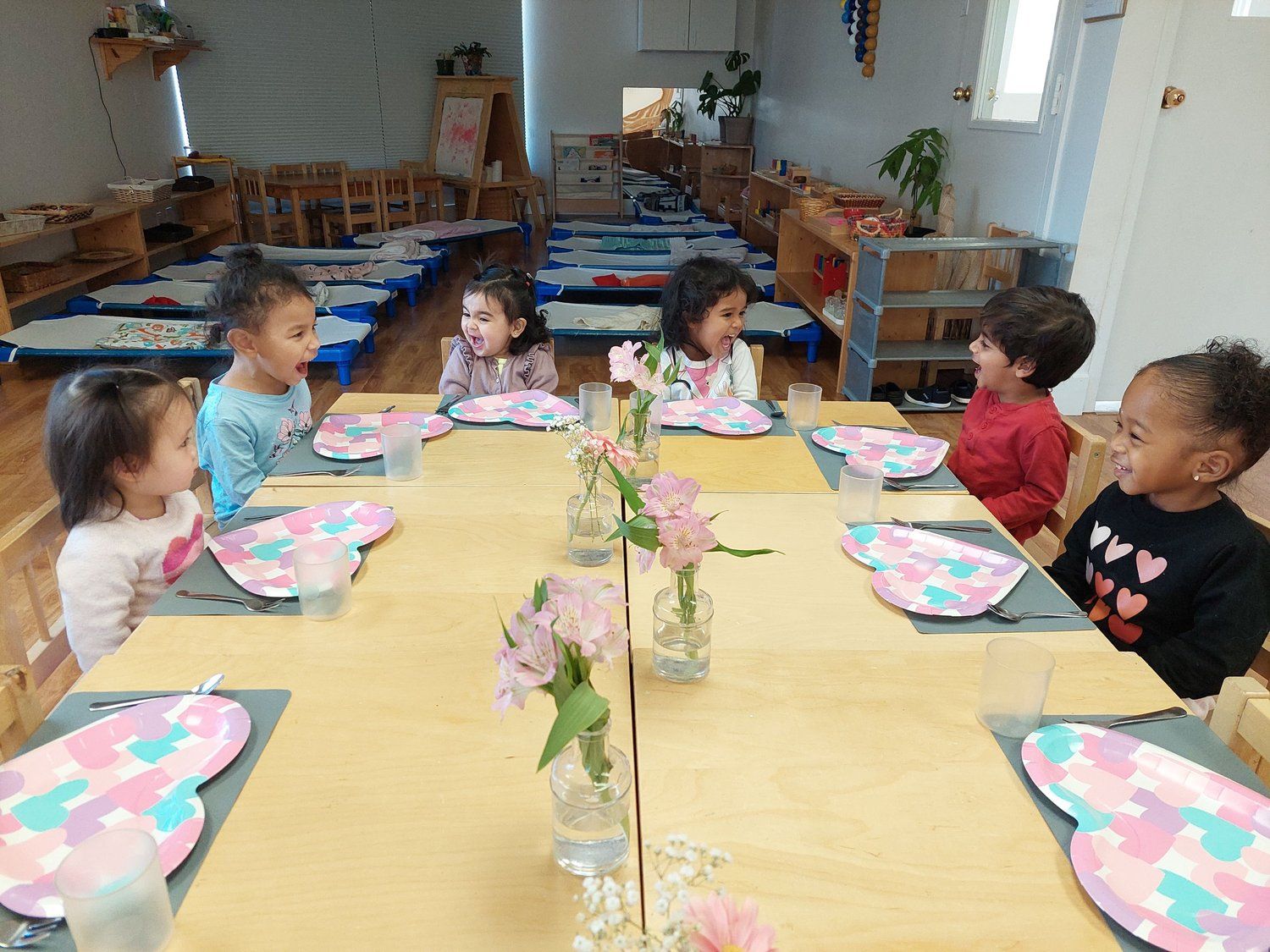 A group of children are sitting at a table with plates and flowers.