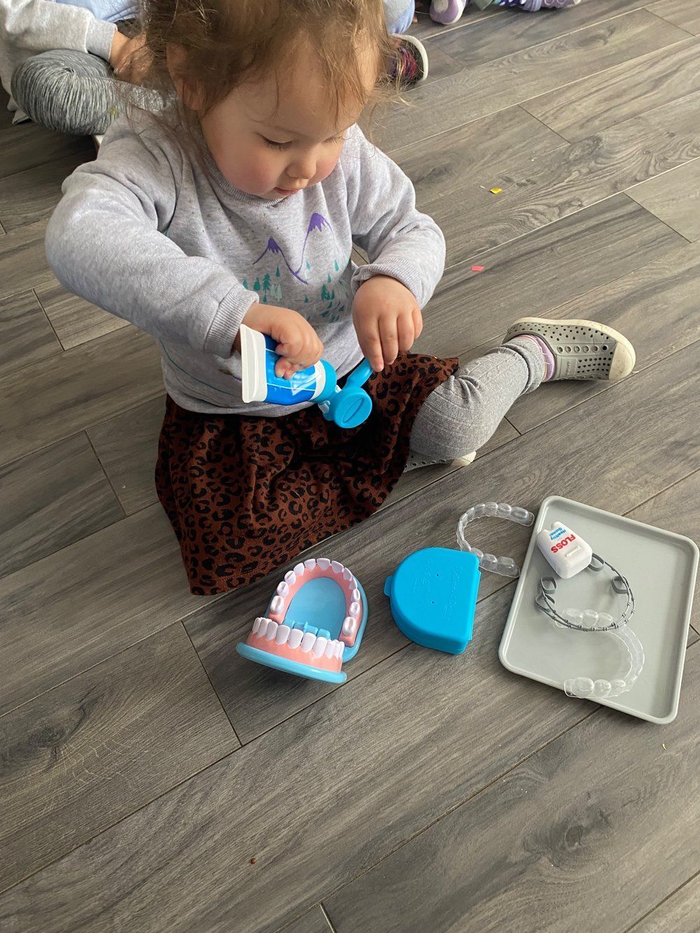 A little girl is sitting on the floor brushing her teeth with a toy toothbrush.