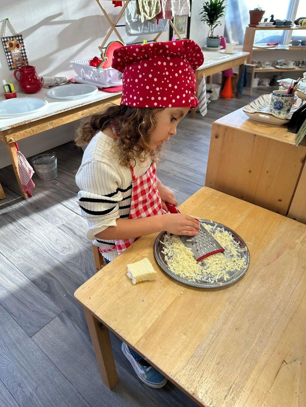 A little girl wearing a chef 's hat and apron is cutting cheese on a plate.