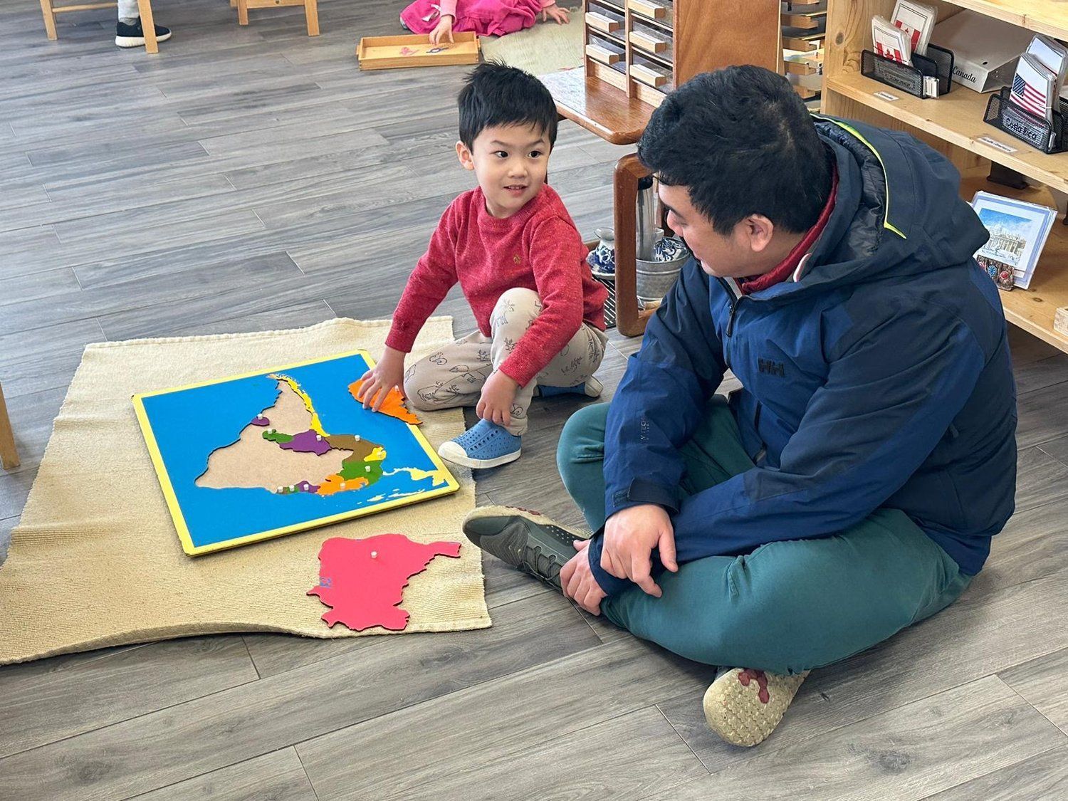 A man and a child are sitting on the floor playing with a puzzle.