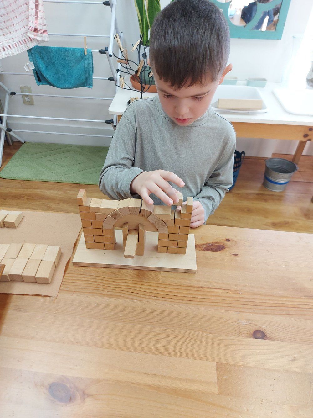 A young boy is playing with wooden blocks on a wooden table.