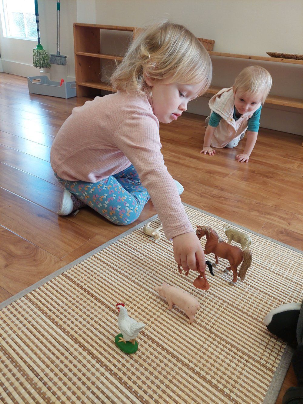 A little girl is playing with toy farm animals on the floor.