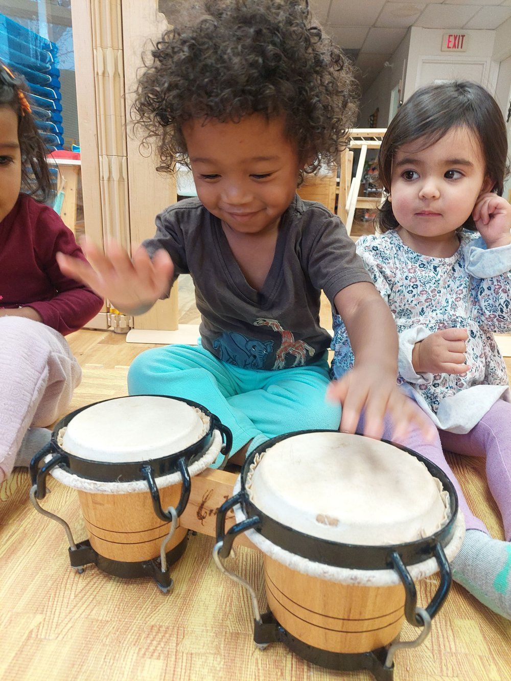 A group of children are sitting on the floor playing drums.