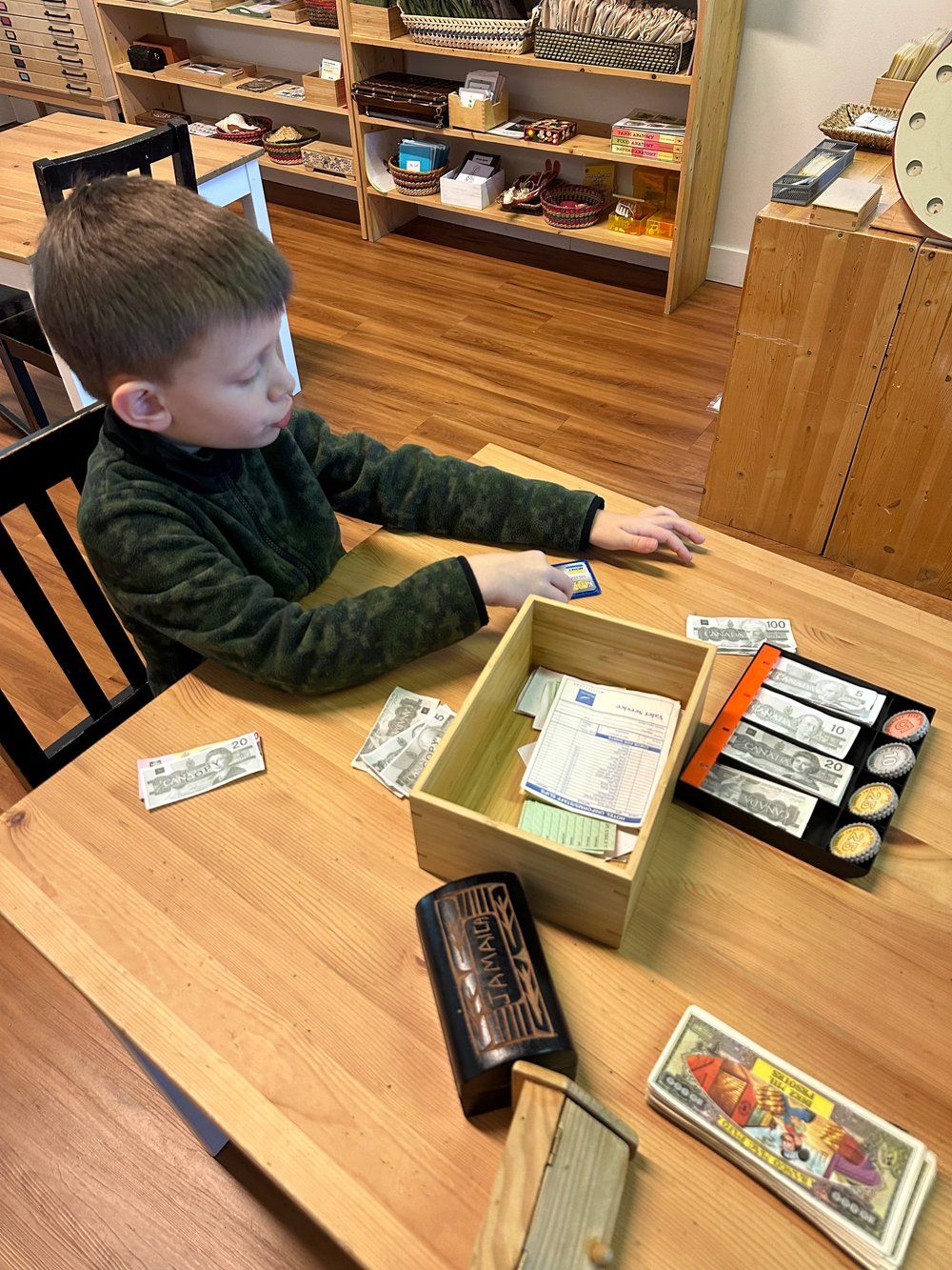 A young boy is sitting at a table with a box of money.