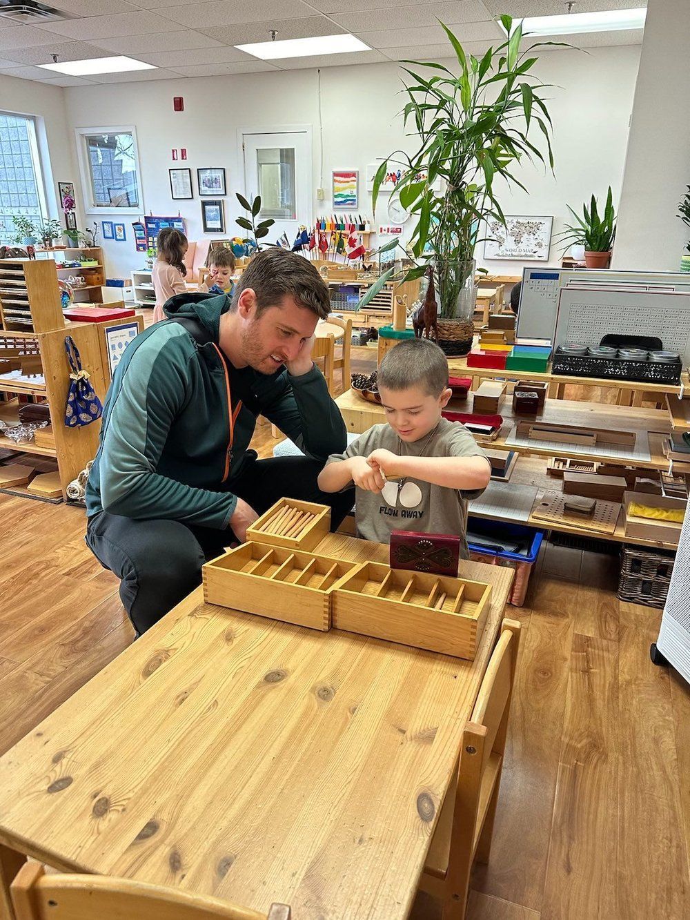 A man and a boy are playing with wooden blocks at a table in a classroom.