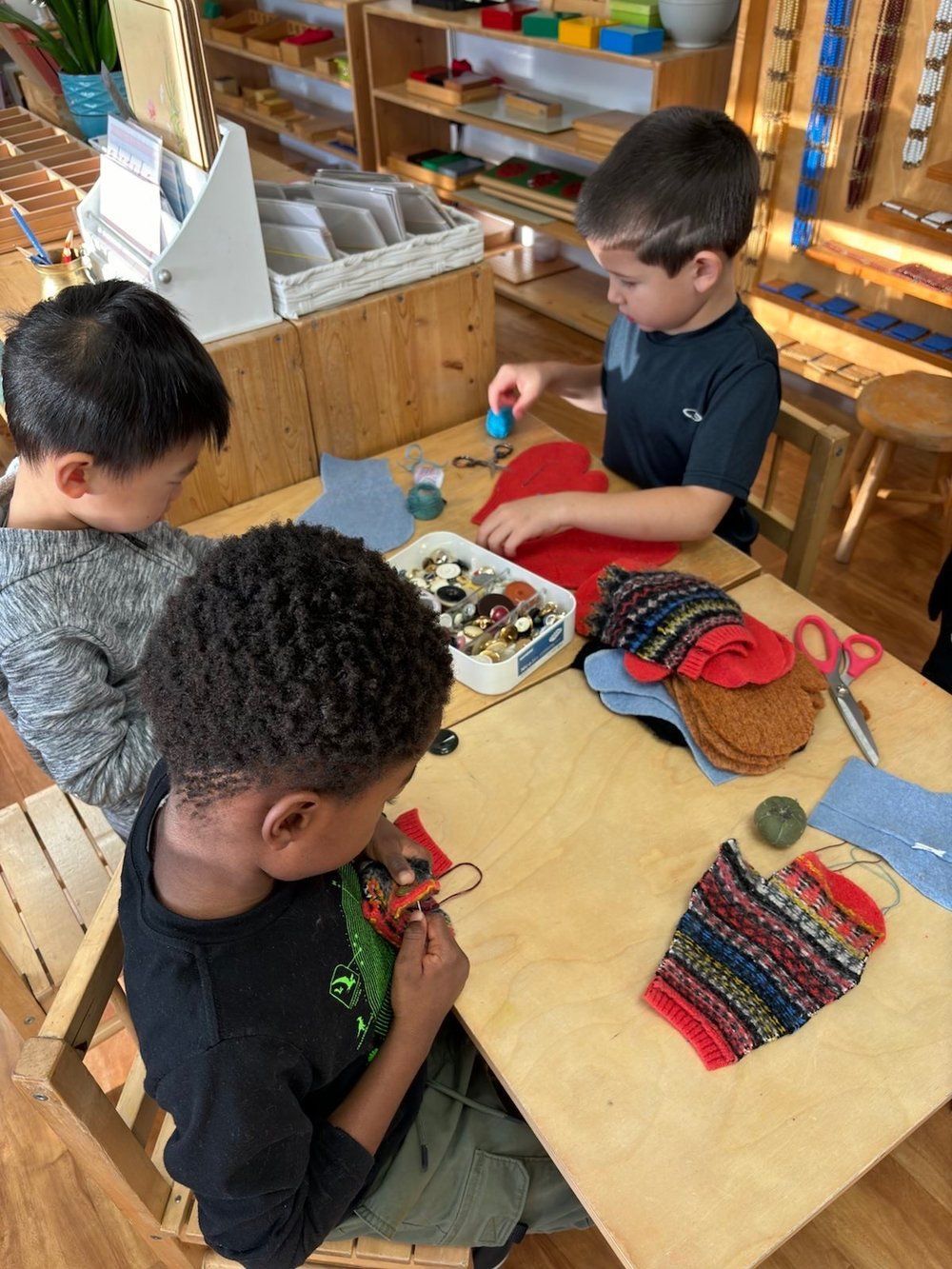 Three young boys are sitting at a table playing with toys.