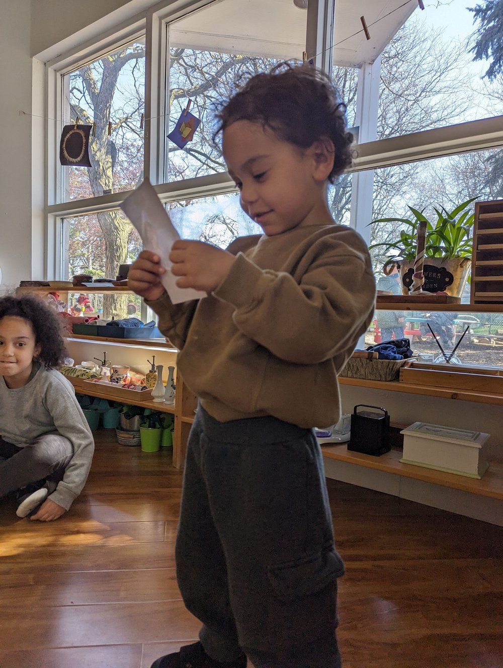 A young boy is standing in front of a window holding a piece of paper.