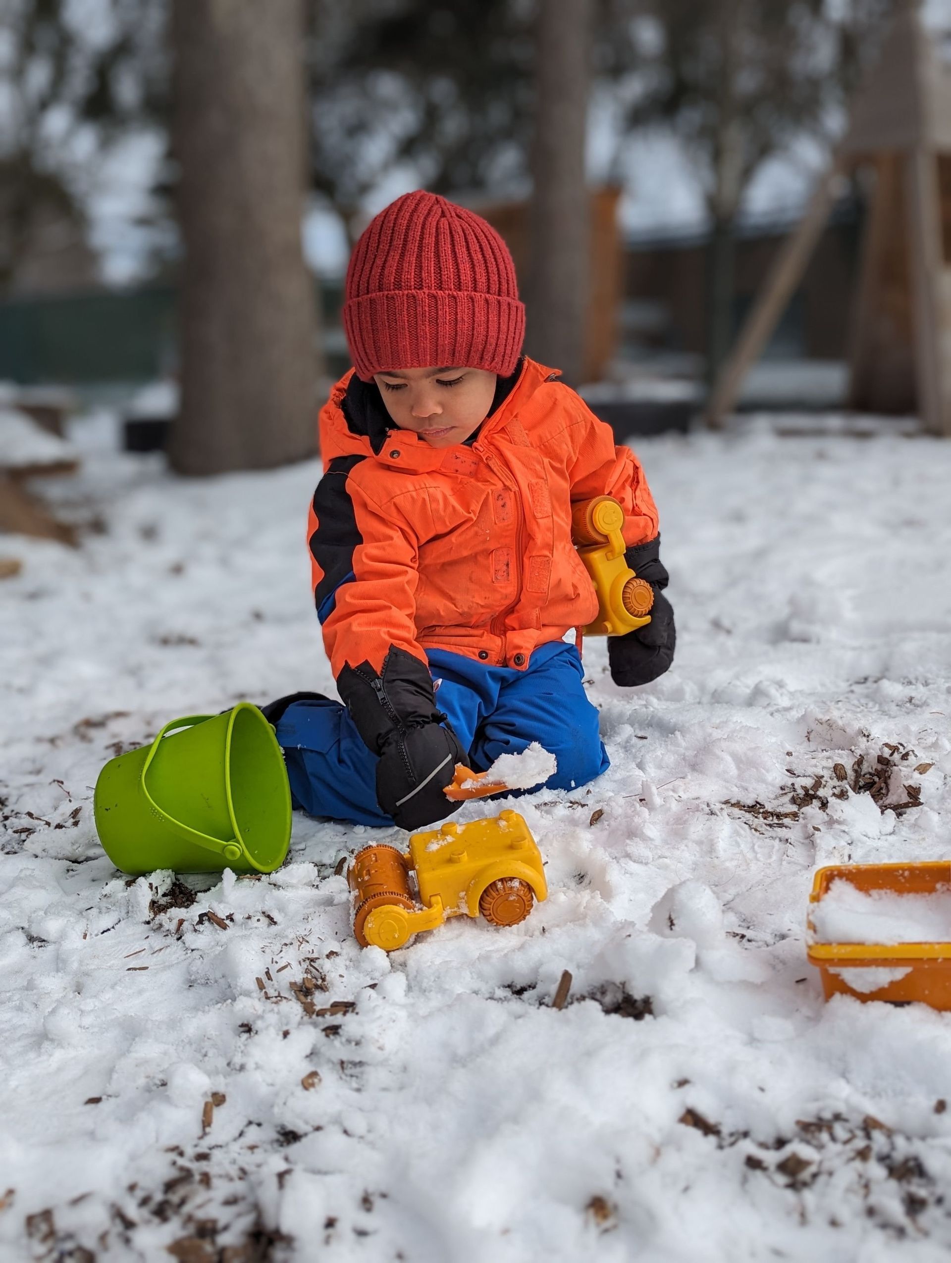 A young boy is playing in the snow with toys.