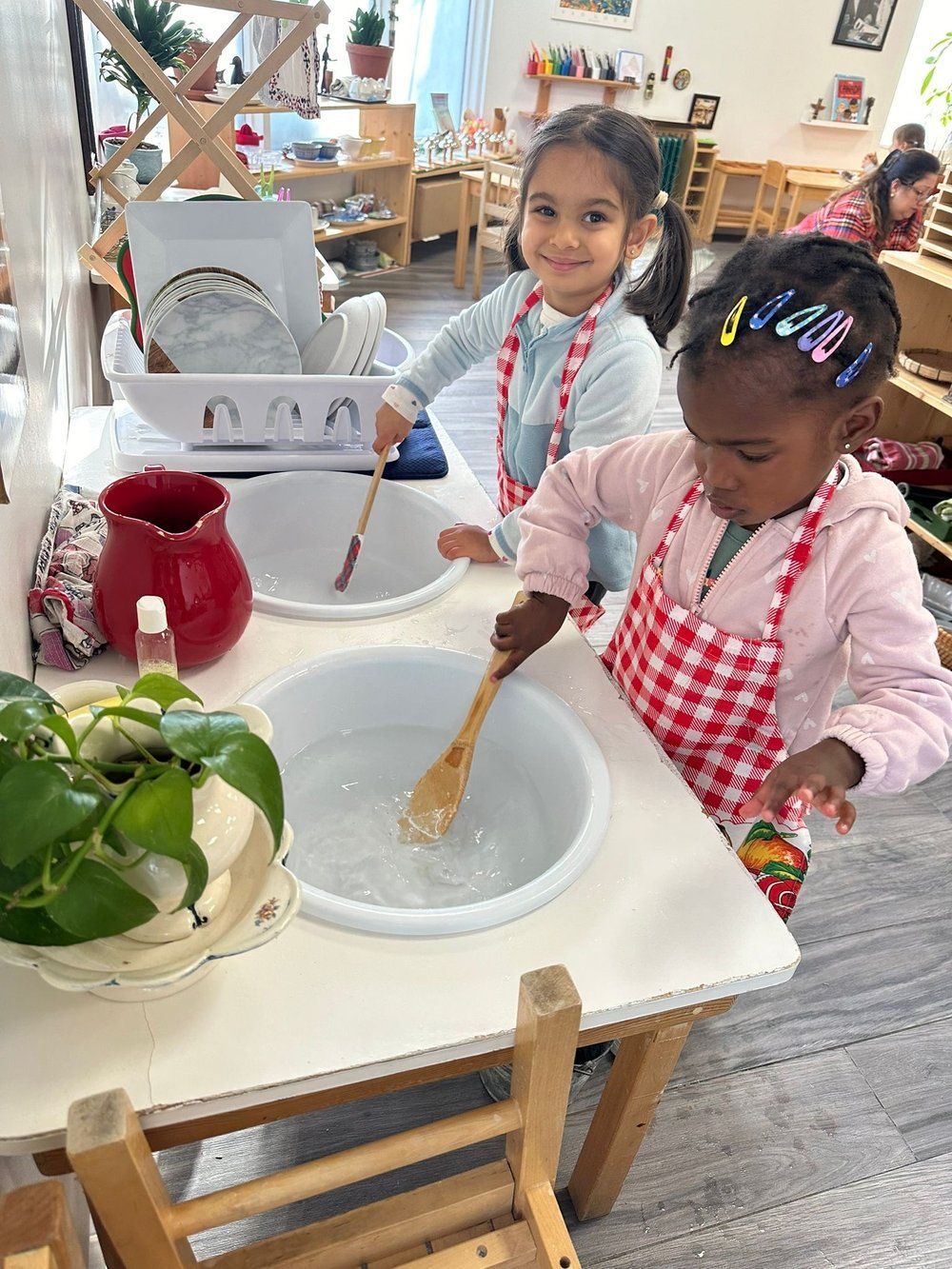 Two little girls are playing with a wooden spoon in a sink.