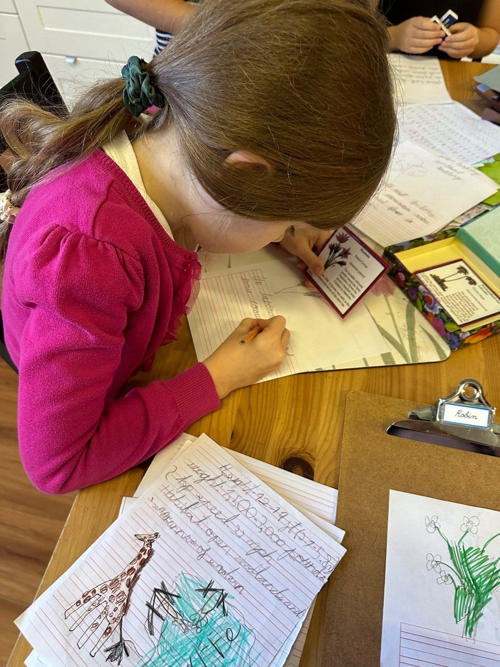 A young girl is sitting at a table writing on a piece of paper.