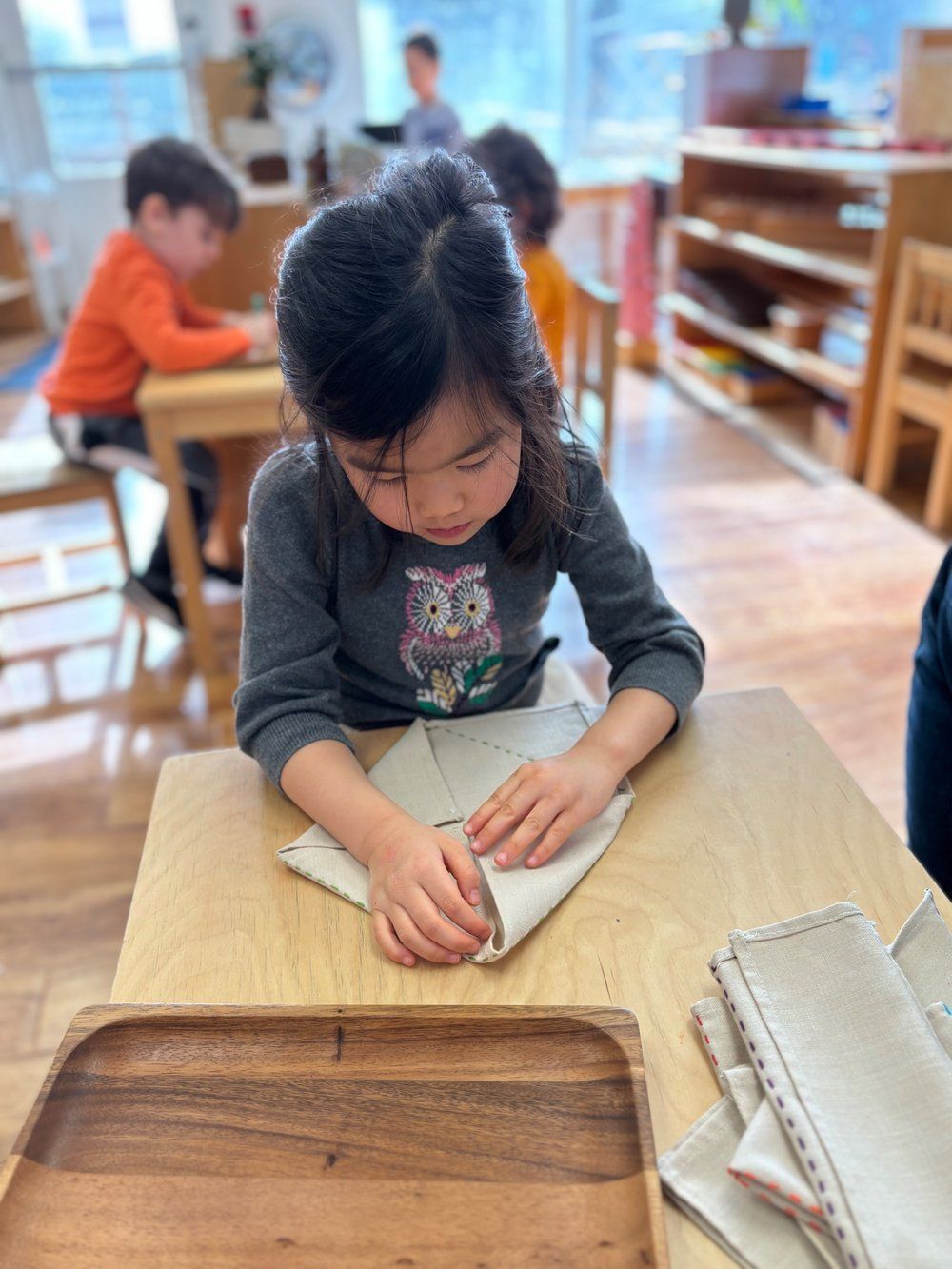A little girl is sitting at a table folding a napkin.
