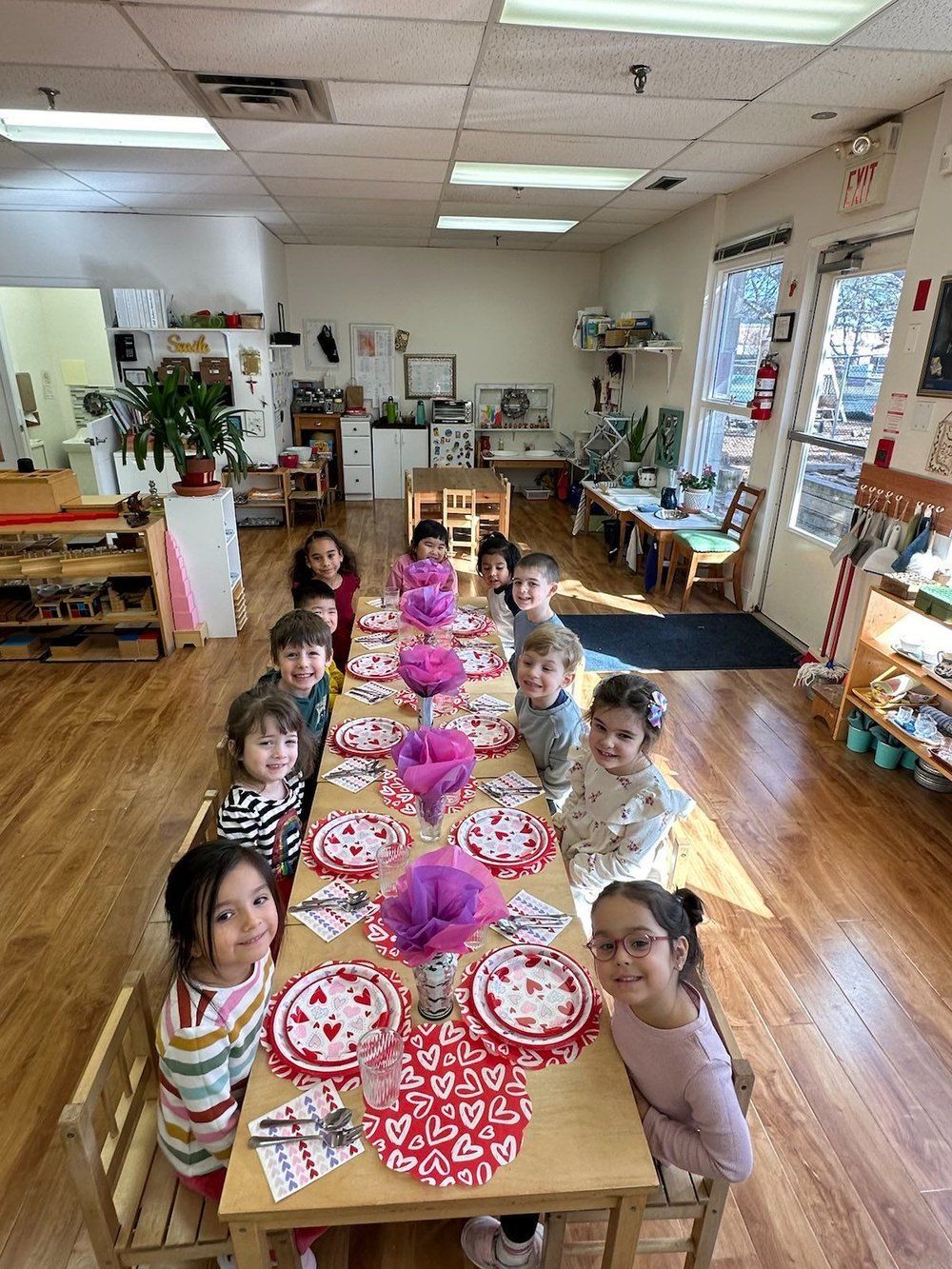 A group of children are sitting at a long table in a classroom.