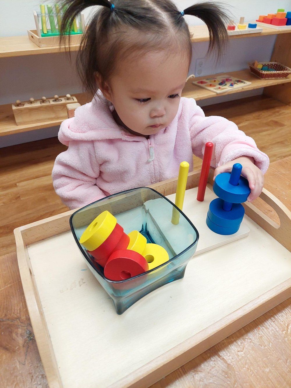 A little girl is playing with a wooden toy on a tray.