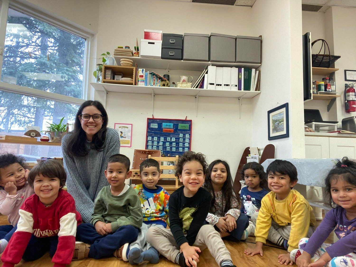 A group of children are sitting on the floor in a classroom with a teacher.